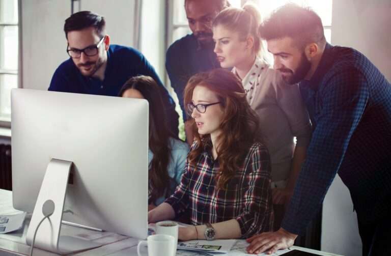 A team of three women and three men working together at the same computer