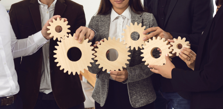 People holding up six wooden gears linked together