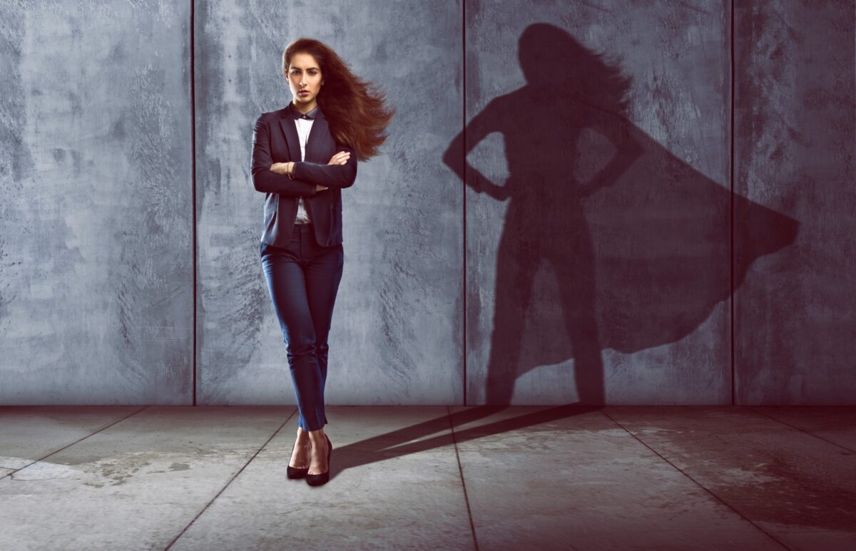 A woman in a suit standing in a power post with her shadow having a cape