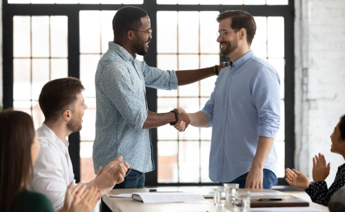 Two men shaking hands and other co-workers clapping that shows a healthy work culture