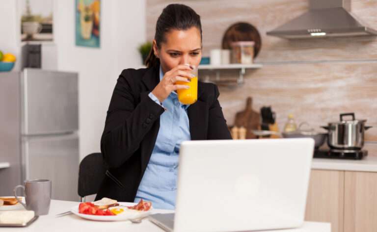 A woman working on her laptop while eating breakfast