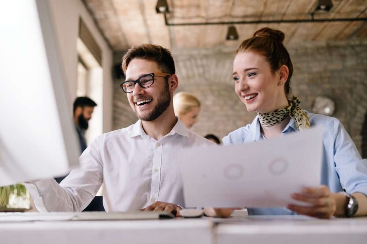 Two coworkers, a man and a woman, talking and looking at a computer