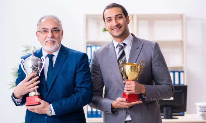 Two businessmen holding up trophies