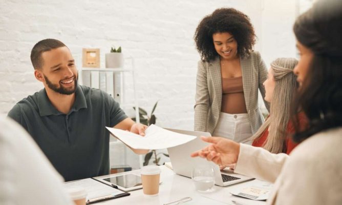 A man handing a document to a woman with two other women working nearby
