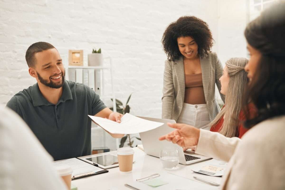 A man handing a document to a woman with two other women working nearby