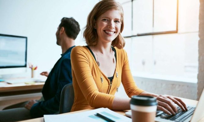 A woman smiling while working with her male coworker working behind her