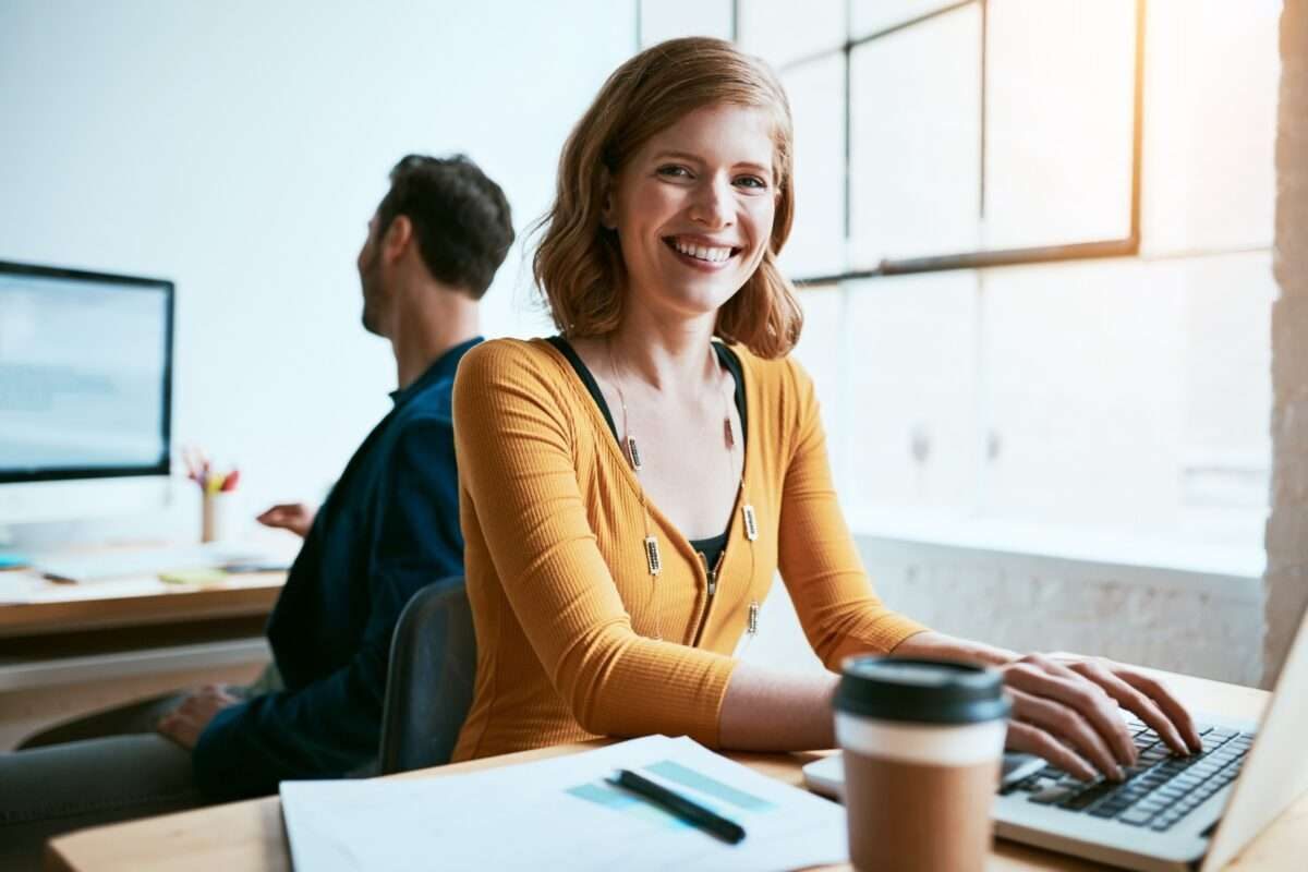 A woman smiling while working with her male coworker working behind her