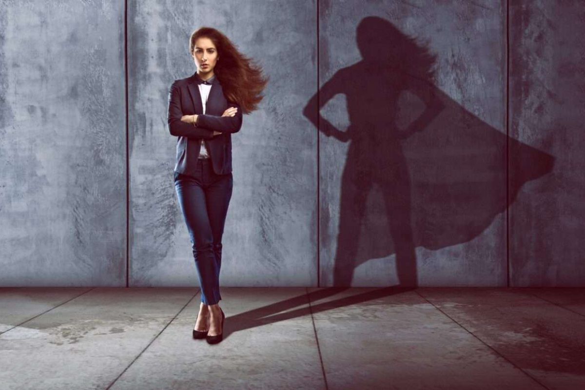 A woman in a suit standing in a power post with her shadow having a cape