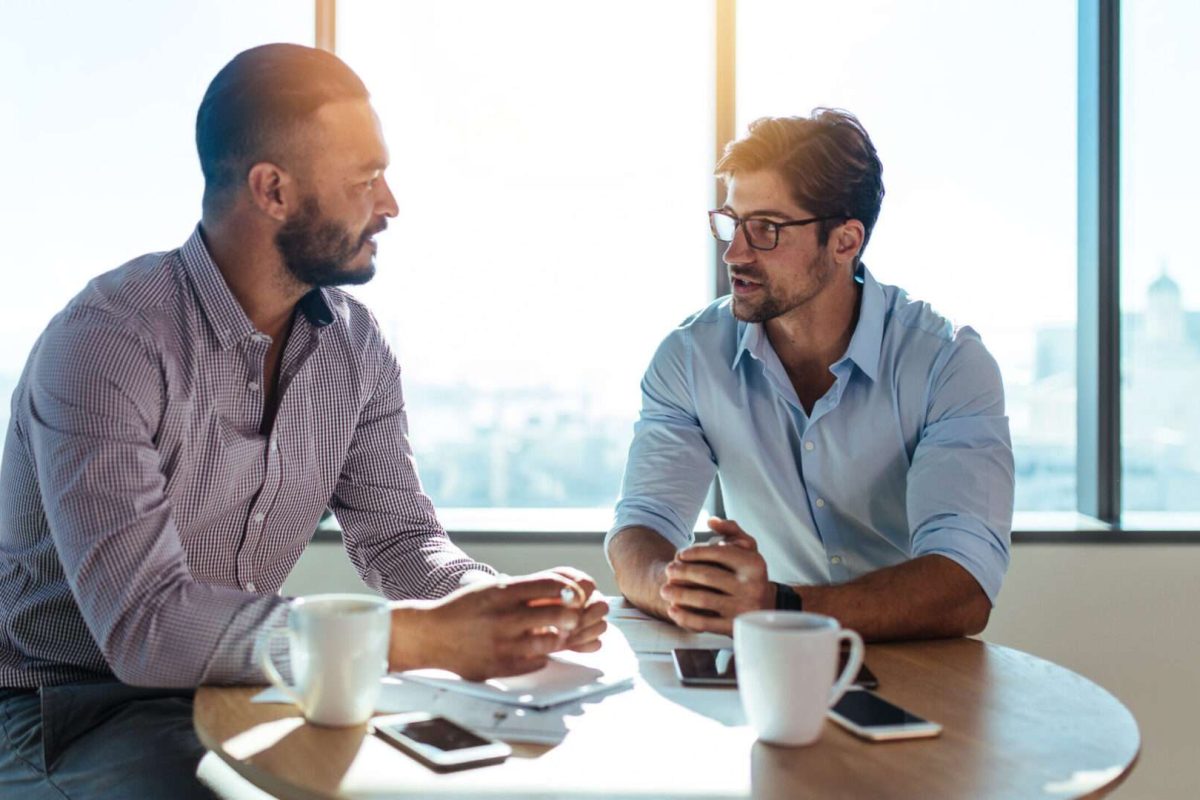 Two men sitting at a table and talking with coffees next to them