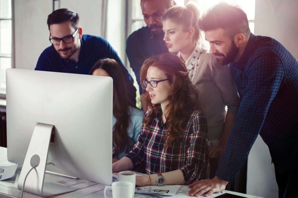 A team of three women and three men working together at the same computer