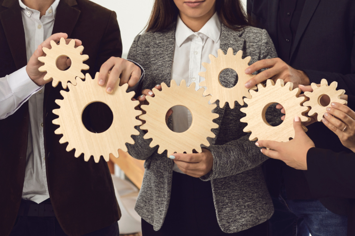 People holding up six wooden gears linked together