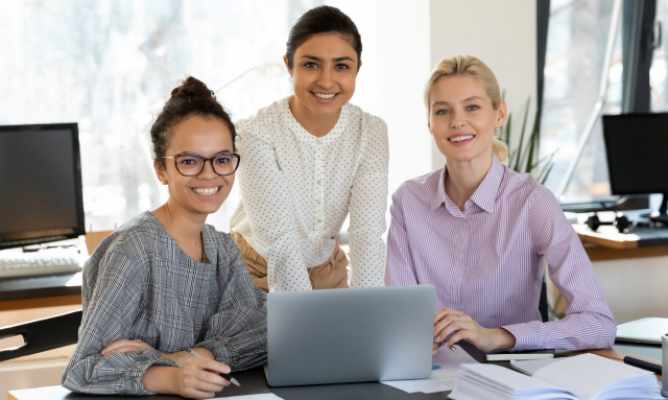 Three women in front of a computer smiling