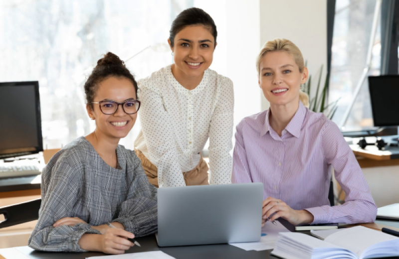Three women in front of a computer smiling
