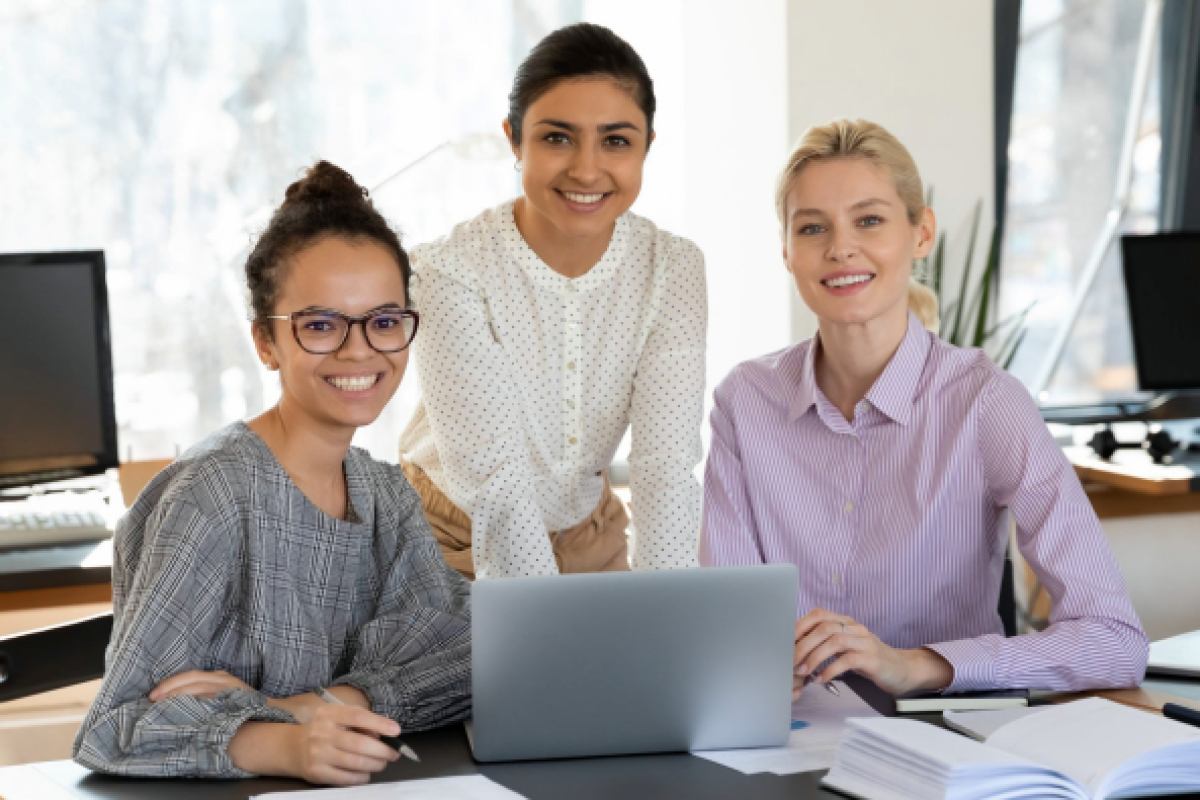Three women in front of a computer smiling