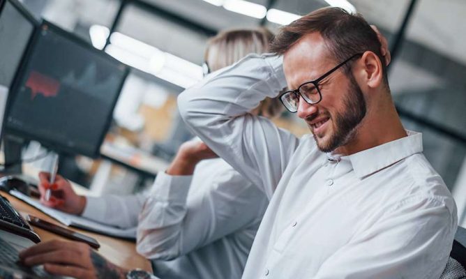 A stressed man rubbing the back of his head at work