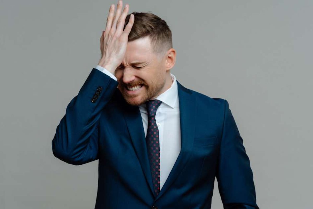A man in a suit slapping his hand against his forehead