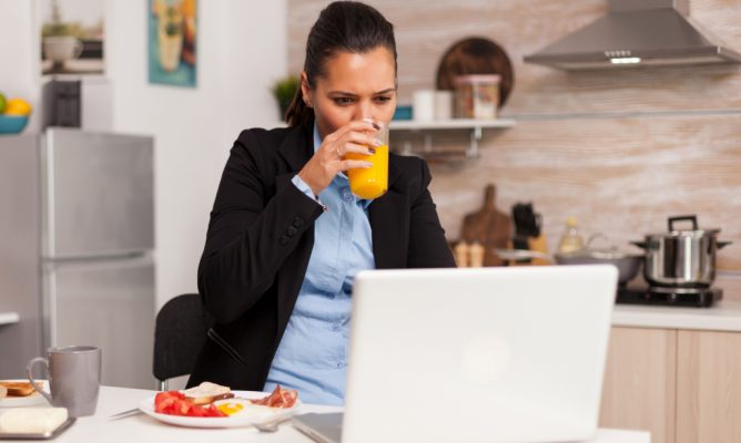 A woman working on her laptop while eating breakfast