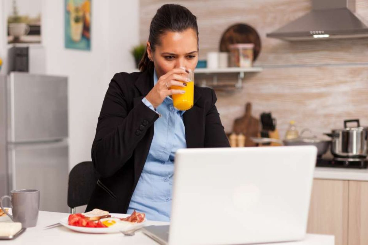 A woman working on her laptop while eating breakfast