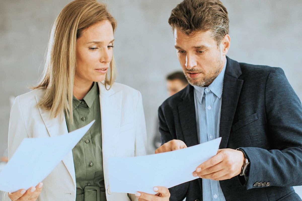 A man and a woman standing next to each other looking at papers
