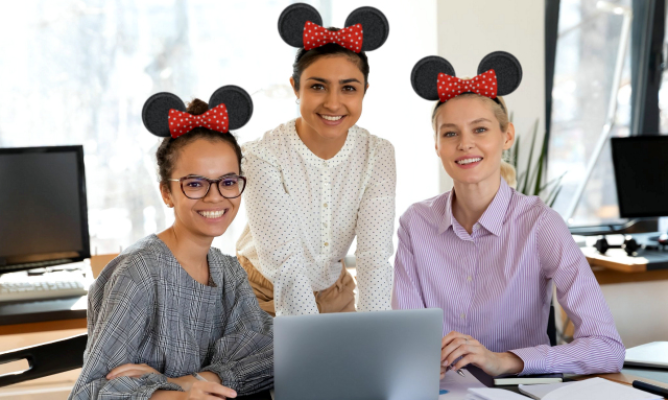 Three woman wearing Mickey Mouse ears smiling in front of a computer
