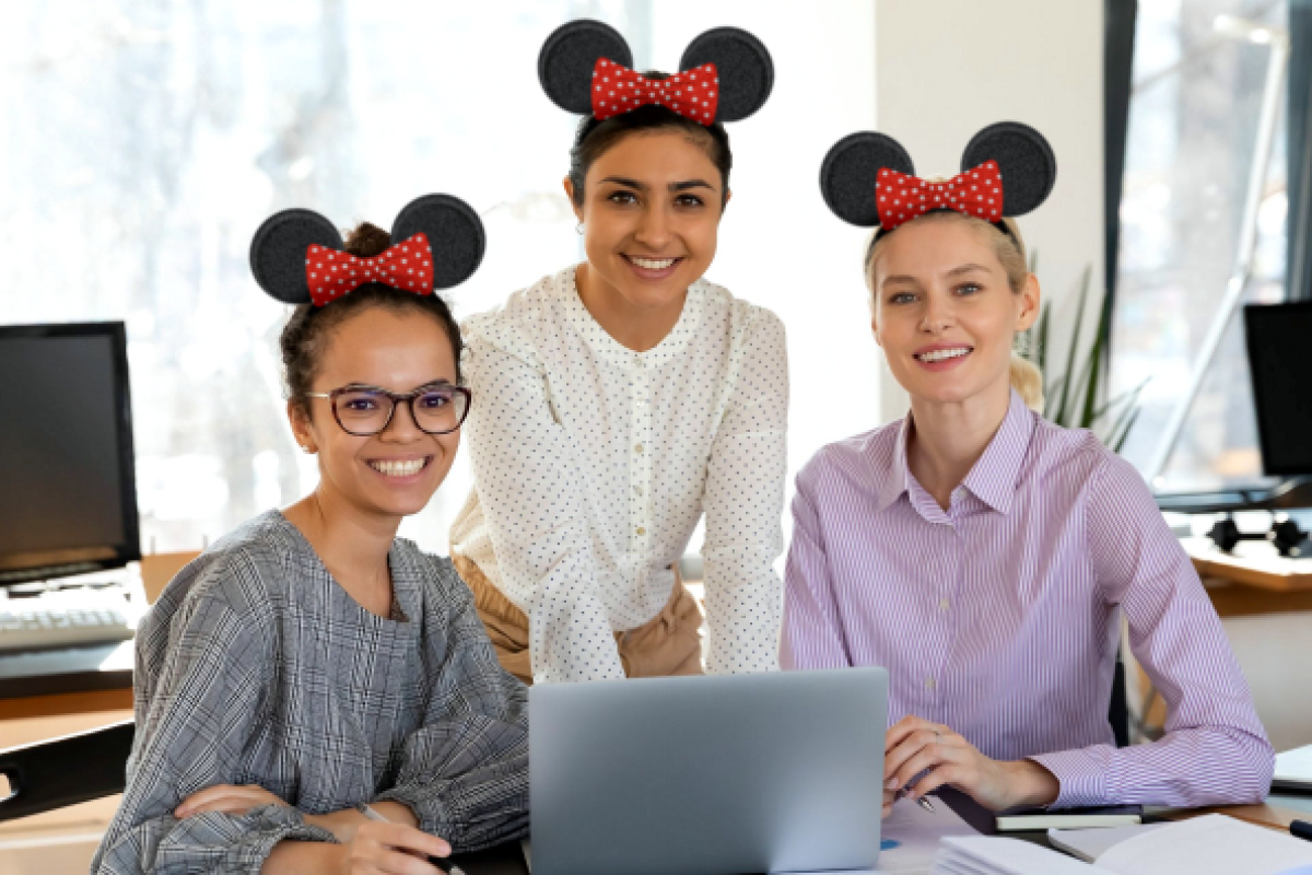 Three woman wearing Mickey Mouse ears smiling in front of a computer