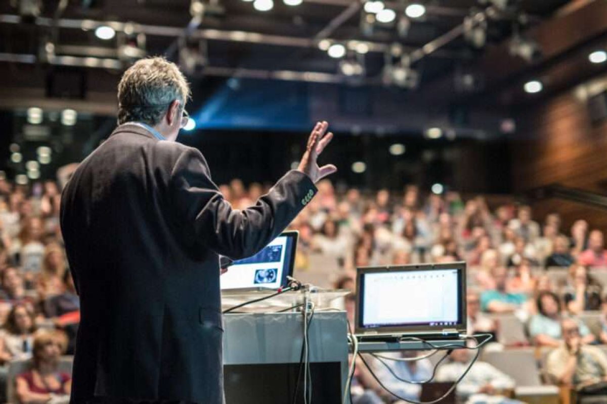 A man presenting in a crowded auditorium