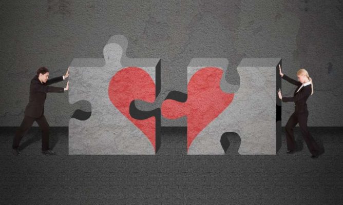 Two people putting together large puzzle pieces that create a heart