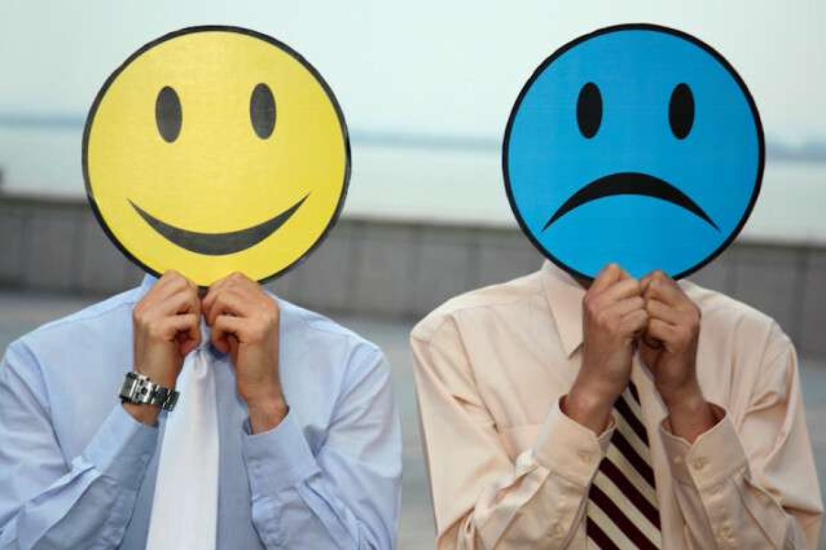 A man holding a smile face sign in front of his face and a man holding a frowny face sign in front of his face
